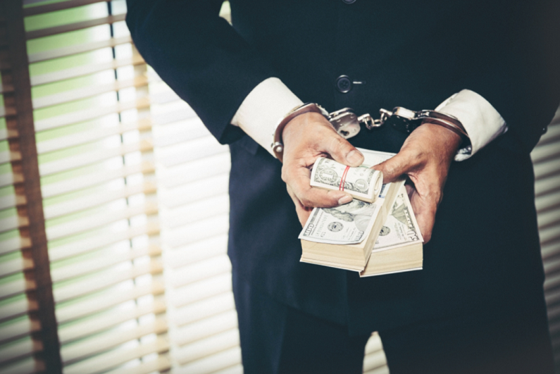 male businessman in handcuffs holding bundles of cash