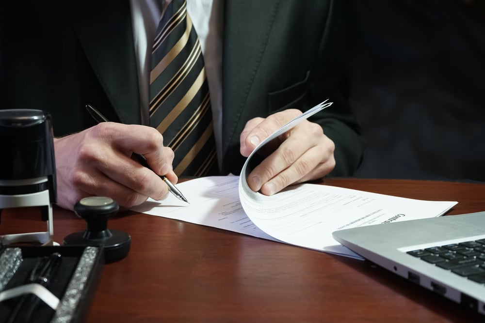 businessperson in suit signing a document at a desk