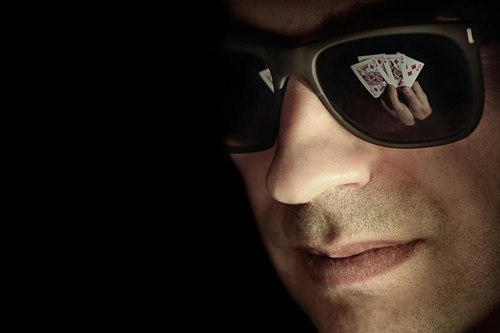 poker cards reflected in male poker player's dark shades