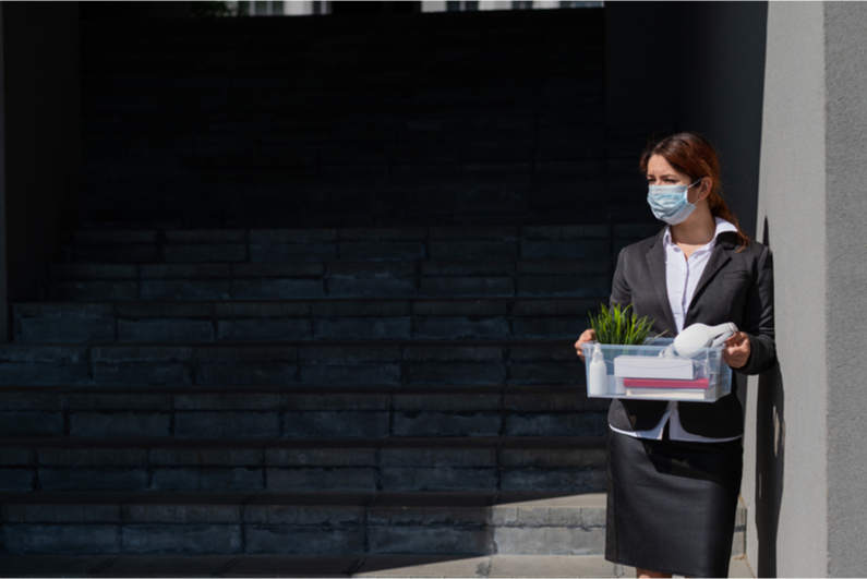 Business woman in mask holding belongings after being laid off