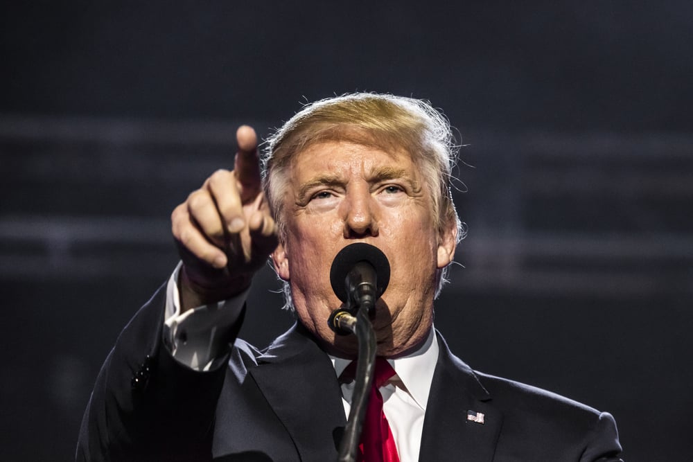 Donald Trump points finger while speaking into a microphone at a rally